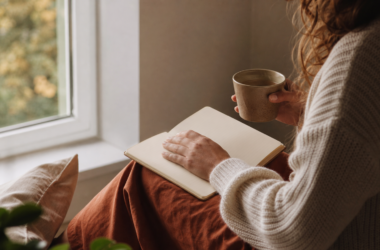 A person reflects beside a window with a journal and warm tea, representing a thoughtful connection to personal motivation.