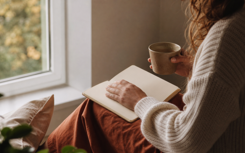 A person reflects beside a window with a journal and warm tea, representing a thoughtful connection to personal motivation.