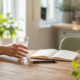 A hand reaches for water beside fresh fruit and an open journal in a bright home kitchen, representing practical daily healthy habits.