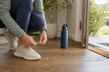 A person ties walking shoes beside an open doorway in the morning, representing a kind and confident first step toward healthy habits.
